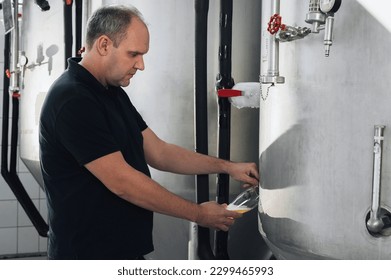 brewer at brewery pours beer into a glass from the tank for inspection - Powered by Shutterstock