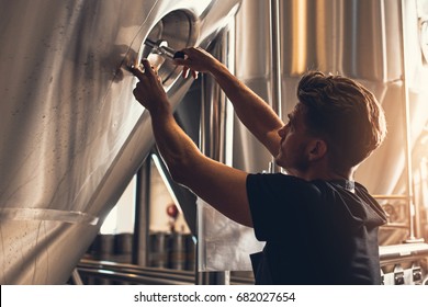 Brewer closing the hatch of brewery tank. Young male employee working in beer manufacturing factory. - Powered by Shutterstock