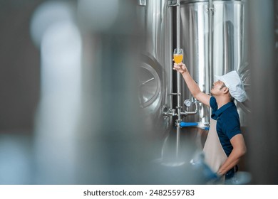 A brewer examining freshly made beer in a glass. Beer craftsman working at his microbrewery holding up beer mug. Manufacturing, food and drink industry concept. - Powered by Shutterstock