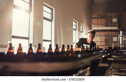 Brewer looking at conveyor with beer bottles. Young man supervising the manufacturing process of beer at brewery factory. - Powered by Shutterstock