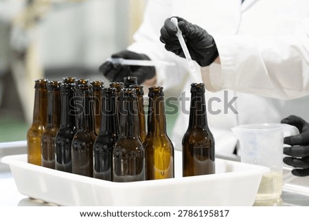 Brewers preparing beer samples using a dropper in the brewery. Workers adding liquid to beer bottles to prepare samples of the craft beer production. Professional laboratory analysis of liquids to monitor the brewing process in the brewery.