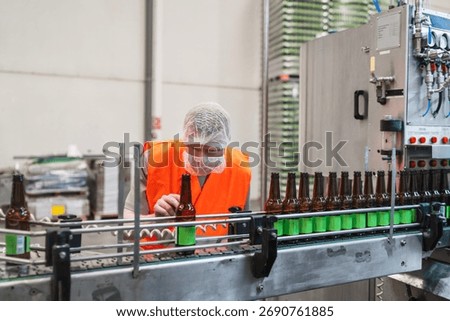 Brewery worker checking amber beer bottles moving on a conveyor belt in a processing plant, ensuring packaging quality