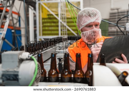 Brewery worker checking beer bottles moving on a conveyor belt at a modern industrial manufacturing plant