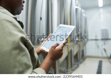 Brewery worker checking charts in application on tablet computer when controlling breer production