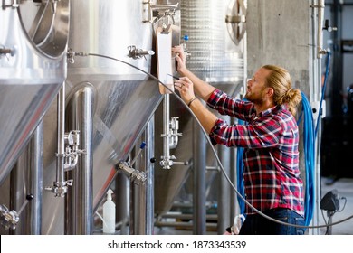 Brewery Worker Checking Fermentation Process In Steel Vat referring to a notepad - Powered by Shutterstock
