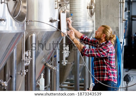 Brewery Worker Checking Fermentation Process In Steel Vat referring to a notepad