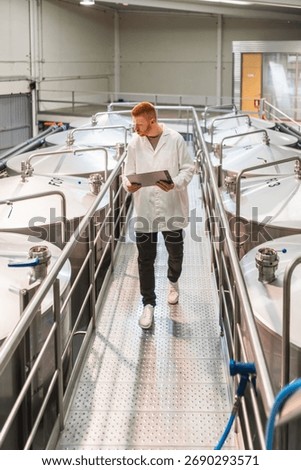 Brewery worker in a lab coat performing quality control checks on fermentation tanks, ensuring beer production standards