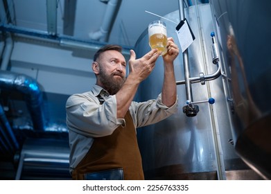 Brewery worker looking at freshly made beer in glass mug - Powered by Shutterstock