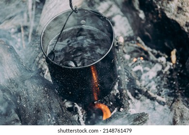 Brewing And Boiling Water In Tourist Pot Over Hearth. Cooking Soup In Metal Pan Over Fire. Survival In Wild, Warming With Hot Drink