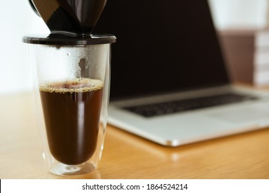 Brewing a filter or drip coffee on the table in office at home with laptop computer in background. Close-up shot of drip coffee in home office.