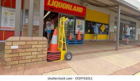 BRIBIE ISLAND, AUSTRALIA - Jan 21, 2021: Woman Wearing Mask Exiting A Liquor Store (liquorland) And A Man Using The Atm Next Door   Pallets, Traffic Cone And Trolley For Loading Outside Store