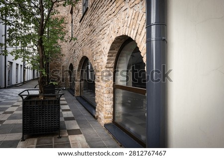Brick Arcade Features Large Arched Windows Beside a Peaceful Pedestrian Walkway With Mature Trees.