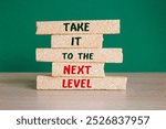 Brick blocks with the message take it to the next level. Beautiful wooden table green background. Business career path for growth and success concept. Copy space.