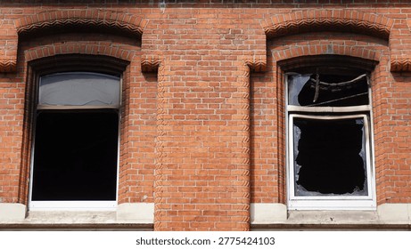 Brick building facade featuring two broken windows with fire damage