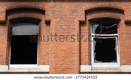 Brick building facade featuring two broken windows with fire damage