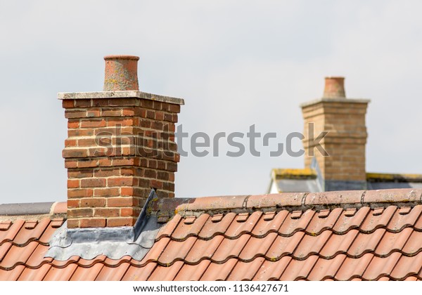 Brick chimney stack on\
modern contemporary house roof top. Urban housing estate tiled roof\
in close-up.