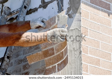 Brick cladding, also called brick veneer is attached to exterior of house made of aerated concrete blocks, construction worker uses tile adhesive.