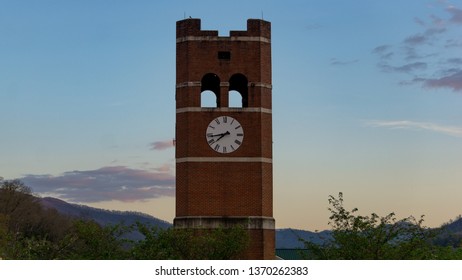 Brick Clock Tower At Sunset In Front Of Foggy Mountains. 