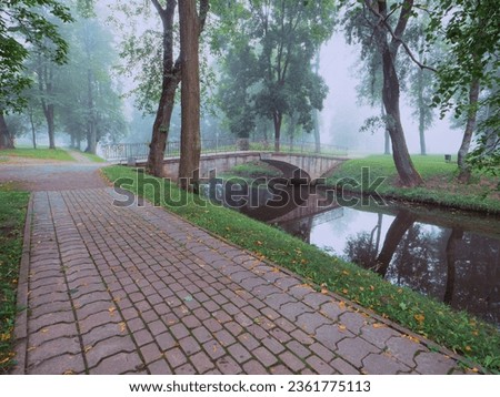 Brick foot path to a small concrete old bridge over a small river in a town forest park in a fog. Mistry surreal calm mood. Relaxing atmosphere and melancholic nature vibe. Imagine de stoc © 