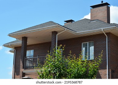 Brick house with asphalt shingles roof, chimney, balcony, rain gutter pipeline and soffit boards. Close up on UPVC Soffit Boards. - Shutterstock ID 2195368787