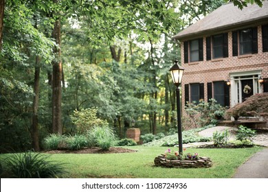 Brick House And Front Yard With Lamp Post In Wooded Area