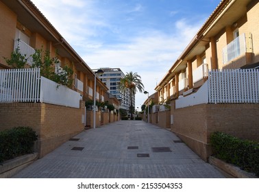 Brick House With Palm Trees In Yard On Street. Home With Apartments At Alboraia, Patacona Beach,  Valencia, Spain. Landscape Design At Suburb Home. Garden With Flowers Near House On Street Courtyard.