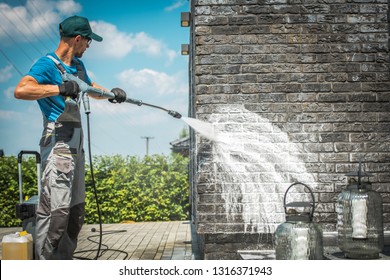 Brick House Wall Pressure Washing With Special Cleaning Detergent. Caucasian Men In His 30s. Taking Care Of The Building Elevation.