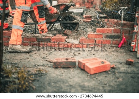 Brick laying bricks building with cement mortar and tools wearing hi vis clothing in cold weather with pep for Saftey 