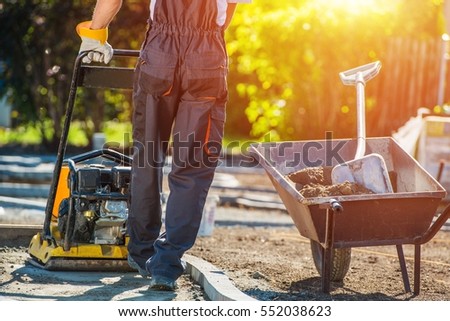 Brick Path Construction. Caucasian Construction Worker with Plate Compactor. Brick Paving Theme.