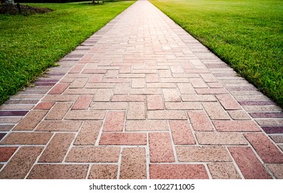 Brick Path Or Sidewalk With Perspective Going Into The Distance With Soft Sunlight Reflecting Of The Bricks. Long Paved Brick Footpath Outside With Grass.