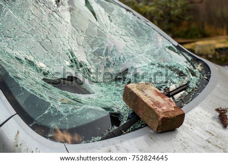 Brick sits on smashed windshield of a car with broken glass everywhere.  The car has been broken into and stolen. Car crime is a problem in United Kingdom
