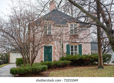 Brick Suburban Home On A Winter Day With Leafless Trees In The Front Yard.