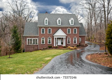 A Brick Two-story House In A Secluded Wooded Setting With An Asphalt Driveway On A Wet, Rainy Winter Day.