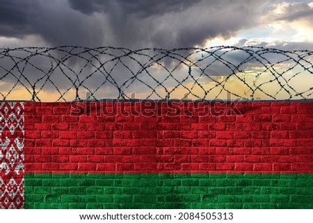 Brick wall with barbed wire in the colors of the state flag of the Republic of Belarus against the background of a stormy sky. Crisis and hybrid war. 