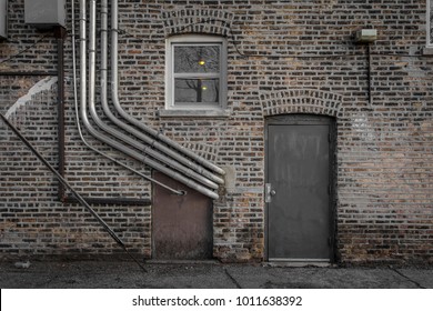 Brick Wall With Pipes And Metal Door In An Alleyway