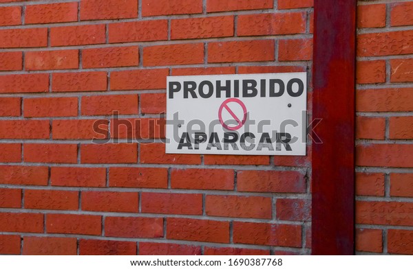 Brick wall with sign in Spanish: Prohibido\
aparcar (English: Parking\
prohibited).