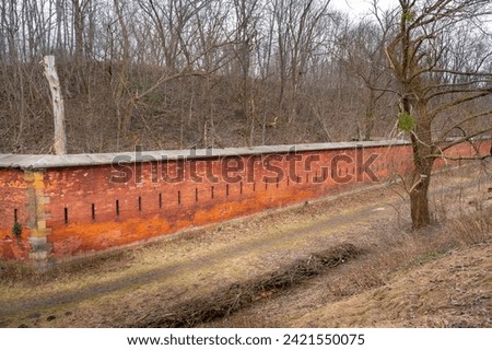 A brick wall surrounding a military fortress from tsar times, a forest, a cut tree