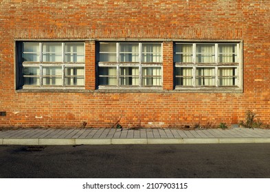 Brick wall with three large windows and curtains. Tiled concrete sidewalk and paved road in front. Background for copy space.