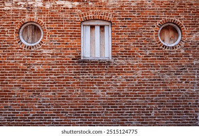 A brick wall with two circular windows and one rectangular window in the center, all with wooden shutters.