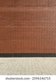 A brick wall with a uniform pattern of reddish-brown bricks. The bricks are neatly aligned in horizontal rows. At the base of the wall, there's a section of a pavement or sidewalk made of square tiles