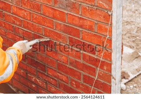 Bricklayer builder applying mortar to brick wall at construction site during daylight
