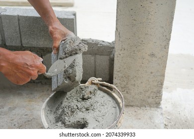 bricklayer or builder hands scooping mixed mortar from bucket put on a piece of brick for installing cement or concrete wall,worker building house with construction material        