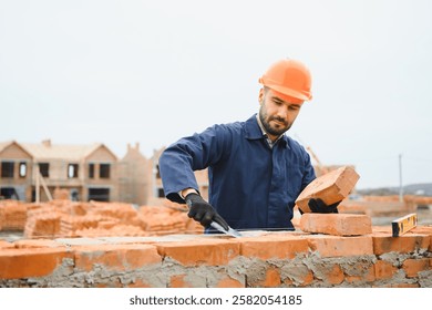 Bricklayer or builder or worker build or bricklaying or laying a stone or brick wall on construction or building site.