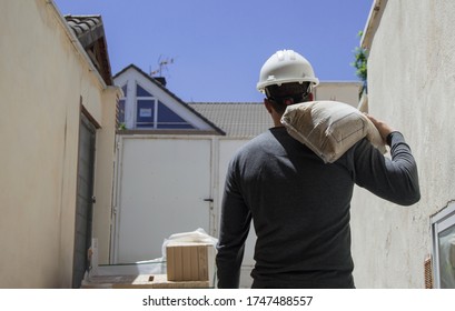 Bricklayer Carrying A Sandbag On His Back And With His Helmet