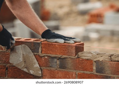 Bricklayer constructing stone wall using stone blocks, cement mortar mix and trowel
