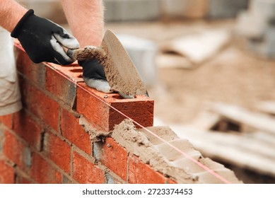 Bricklayer constructing stone wall using stone blocks, cement mortar mix and trowel
