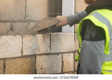 Bricklayer constructing stone wall using stone blocks, cement mortar mix and trowel