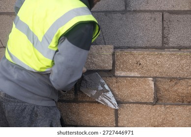 Bricklayer constructing stone wall using stone blocks, cement mortar mix and trowel