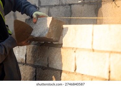 Bricklayer constructing stone wall using stone blocks, cement mortar mix and trowel