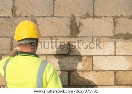Bricklayer constructing stone wall using stone blocks, cement mortar mix and trowe